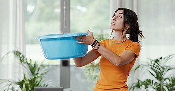 Woman holding bucket inside catching water leak from damaged roof